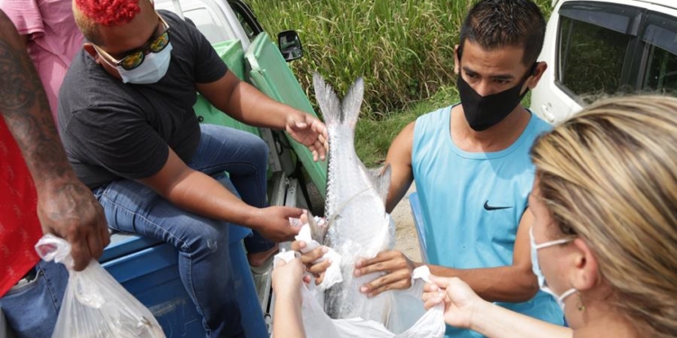 El pescador venezolano Carlos Hernández (i) regala bolsas de pescado a personas de familias necesitadas este domingo en St. Helena, Trinidad y Tobago.