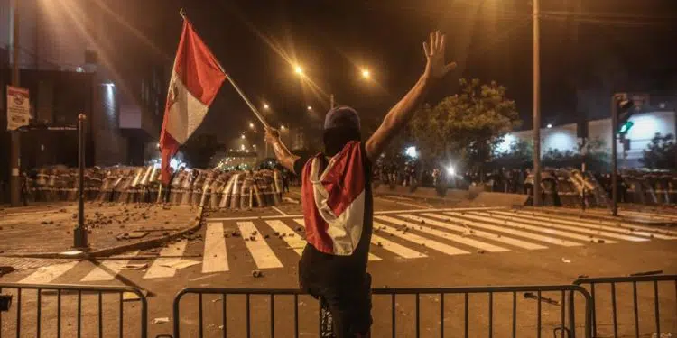 Un manifestante ondea una bandera frente a un cerco policial hoy, en Lima (Perú). Miles de peruanos desafiaron este martes el toque de queda ordenado por el presidente Pedro Castillo para Lima y su vecina provincia de Callao y se manifestaron en la capital para pedir la renuncia del mandatario. EFE/ Aldair Mejía