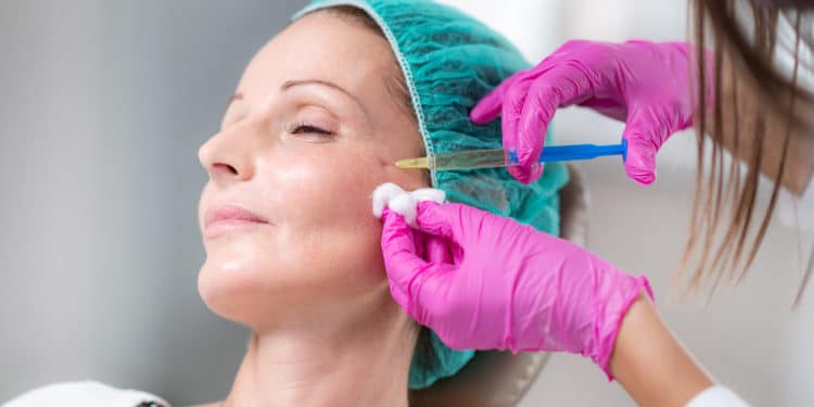 Anti-Aging Treatment. Doctor with surgical gloves marking senior women’s face for hyaluronic injection treatment